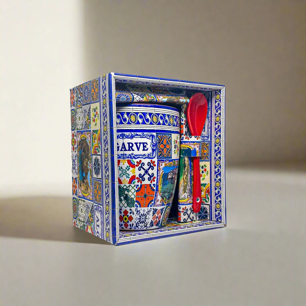A colorful ceramic coffee mug with intricate patterns and "ALGARVE" text is displayed in a matching decorative box. A red spoon is attached to the set. The box and mug feature a vibrant mosaic design, inspired by Portugal's rich artistry, creating a traditional and artistic appeal.