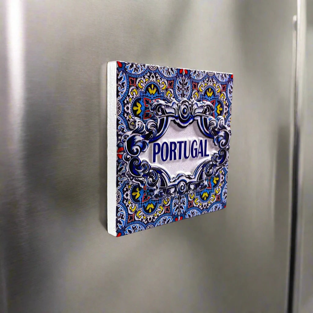 A decorative tile magnet adorned with detailed blue, yellow, and white patterns, with "PORTUGAL" prominently displayed in the center. The ornate floral and geometric designs evoke the charm of traditional Portuguese azulejos, making it a lovely souvenir.
