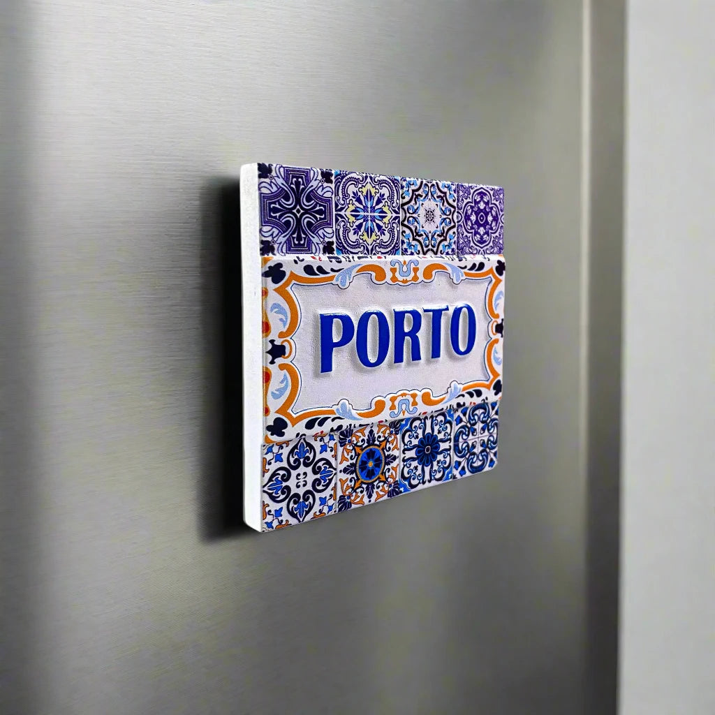 A decorative tile magnet showcasing the word "PORTO" in blue, framed by detailed designs in blue, white, and yellow. The magnet highlights floral and geometric patterns in a traditional Portuguese azulejo style, making it an ideal keepsake from Porto.
