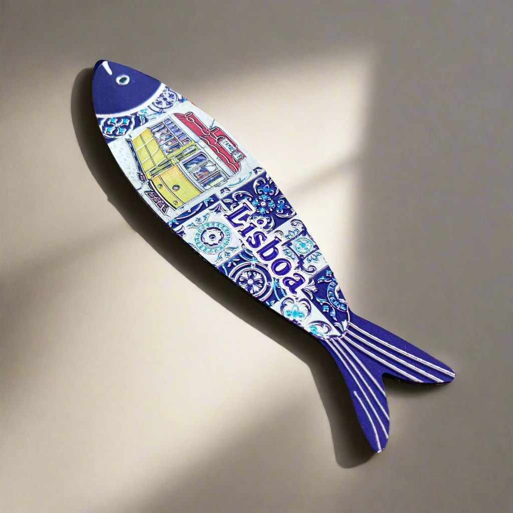 A fish-shaped ornament and magnet displays a Lisbon tram design on its body. The fish features a blue head and tail, with intricate blue and white tile patterns along its center. The word "Lisboa" is prominently featured beside the tram illustration, beautifully capturing the essence of Portugal.