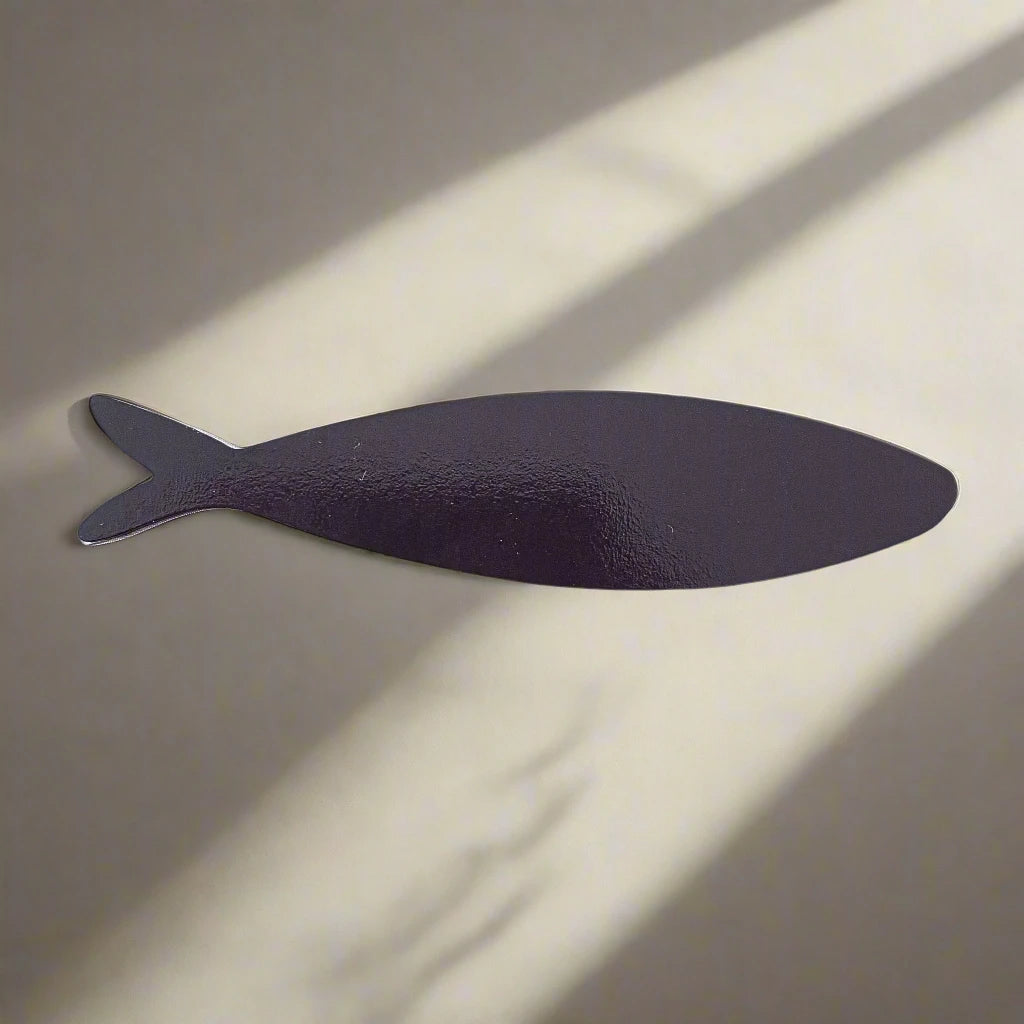 A minimalist image featuring a simple silhouette of a fish against a plain background with light and shadow patterns that mimic sunlight streaming through a window. The dark fish silhouette evokes the clean, uncluttered aesthetic reminiscent of Portugal, making it an ideal magnet souvenir.