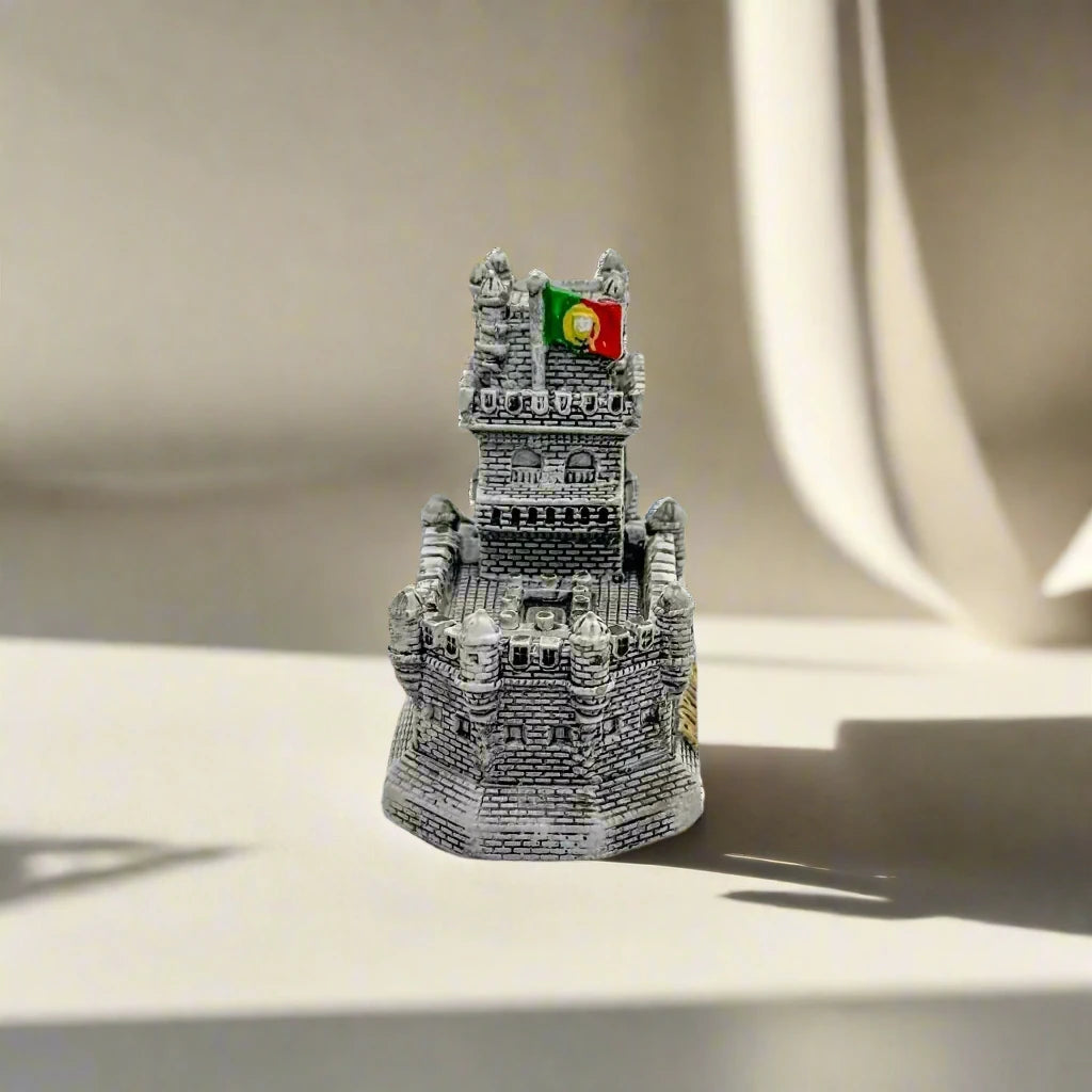 A detailed miniature replica of Lisbon's iconic Belem Tower is displayed, with the word "PORTUGAL" elegantly inscribed in gold at the base. The intricate design of the tower stands out against a clean, white background.