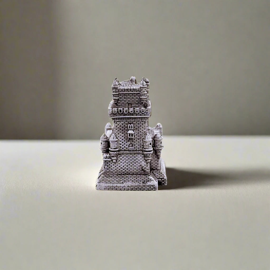 A small, intricately crafted replica of Lisbon's Belem Tower is shown with "PORTUGAL" inscribed in gold at the base. Set against a white background, the detailed architecture is beautifully highlighted.