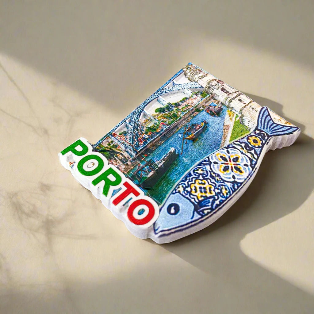 A Porto souvenir featuring the city's name in bold green, white, and red letters, along with an image of boats sailing on a river beneath a bridge. A decorative fish adorned with traditional Portuguese tile patterns adds a cultural touch, while a subtle reference to the iconic Clérigos Tower completes this charming memento.