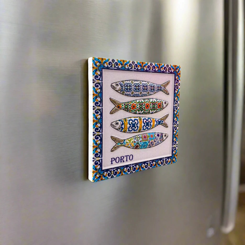 A decorative tile magnet showcasing four vibrant sardines adorned with elaborate patterns in blue, green, yellow, and red. Each sardine boasts a distinct design. The tile souvenir features a blue and yellow floral border and displays the word "PORTO" at the bottom.