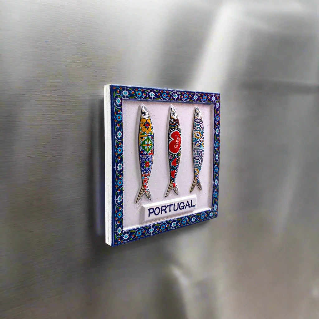 A charming magnet depicting three illustrated sardines, each decorated with unique, colorful patterns reminiscent of traditional tile designs. The sardines are set against a blue, white, and green patterned border, with the word "PORTUGAL" elegantly displayed at the bottom, making it an ideal keepsake.