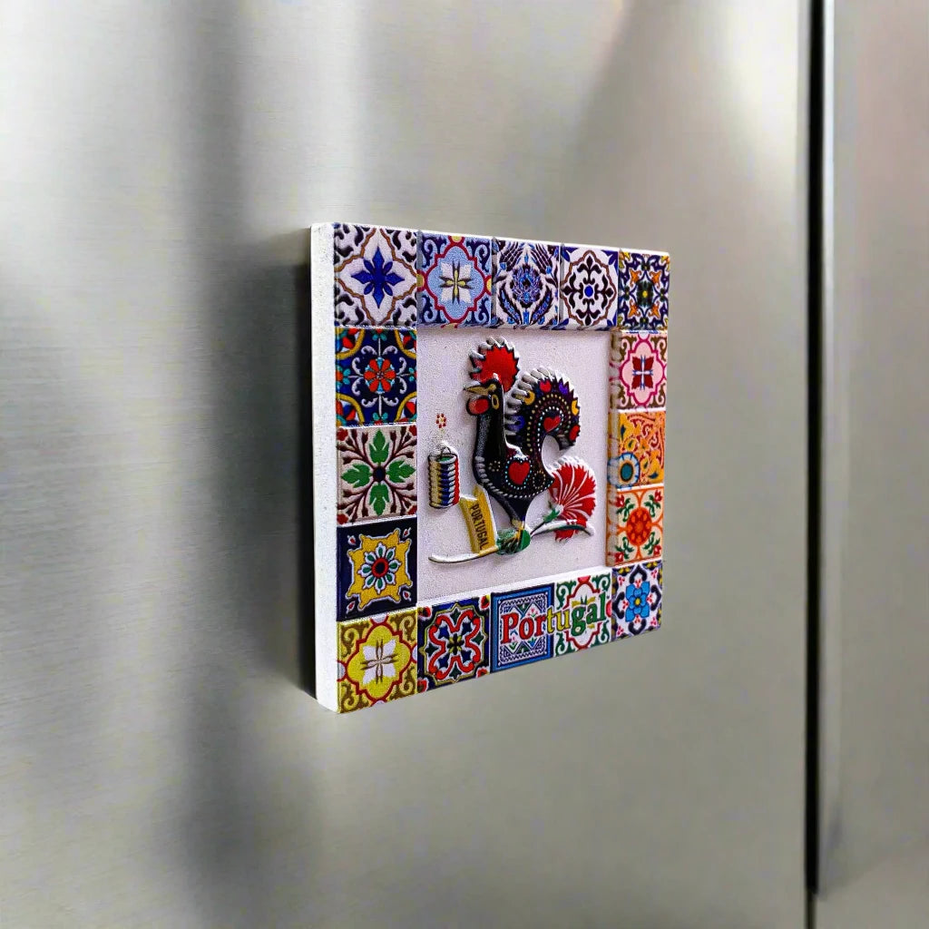 A lively square ceramic tile magnet, ideal as a souvenir, showcasing a traditional Portuguese rooster in the center, framed by detailed floral and geometric patterns. The word "Portugal" is elegantly displayed at the bottom, with vibrant blue, yellow, red, and green hues decorating the border. A functional and decorative keepsake!