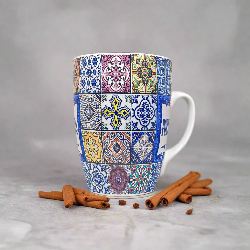 A vibrant ceramic coffee mug with a mosaic tile pattern and the word "PORTUGAL" prominently displayed in the center. The mug showcases intricate blue and yellow designs inspired by traditional Portuguese tiles and includes a small blue ceramic spoon attached to the handle, making it a unique souvenir.
