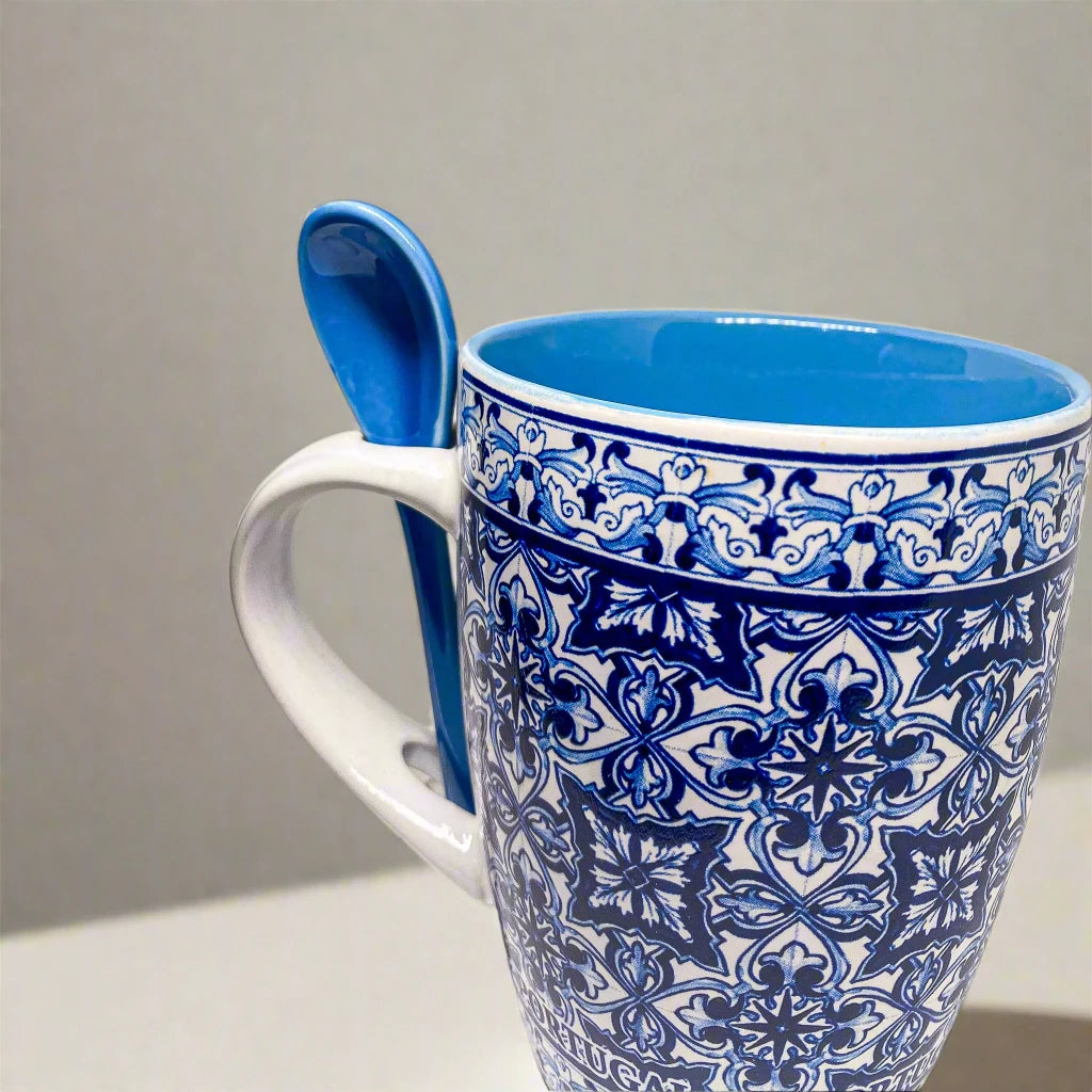 This ceramic coffee mug, adorned with blue and white traditional Portuguese tile motifs, features the word "PORTUGAL" around its base. It includes a coordinating blue spoon that fits neatly into a slot on the handle, combining elegance with practicality.