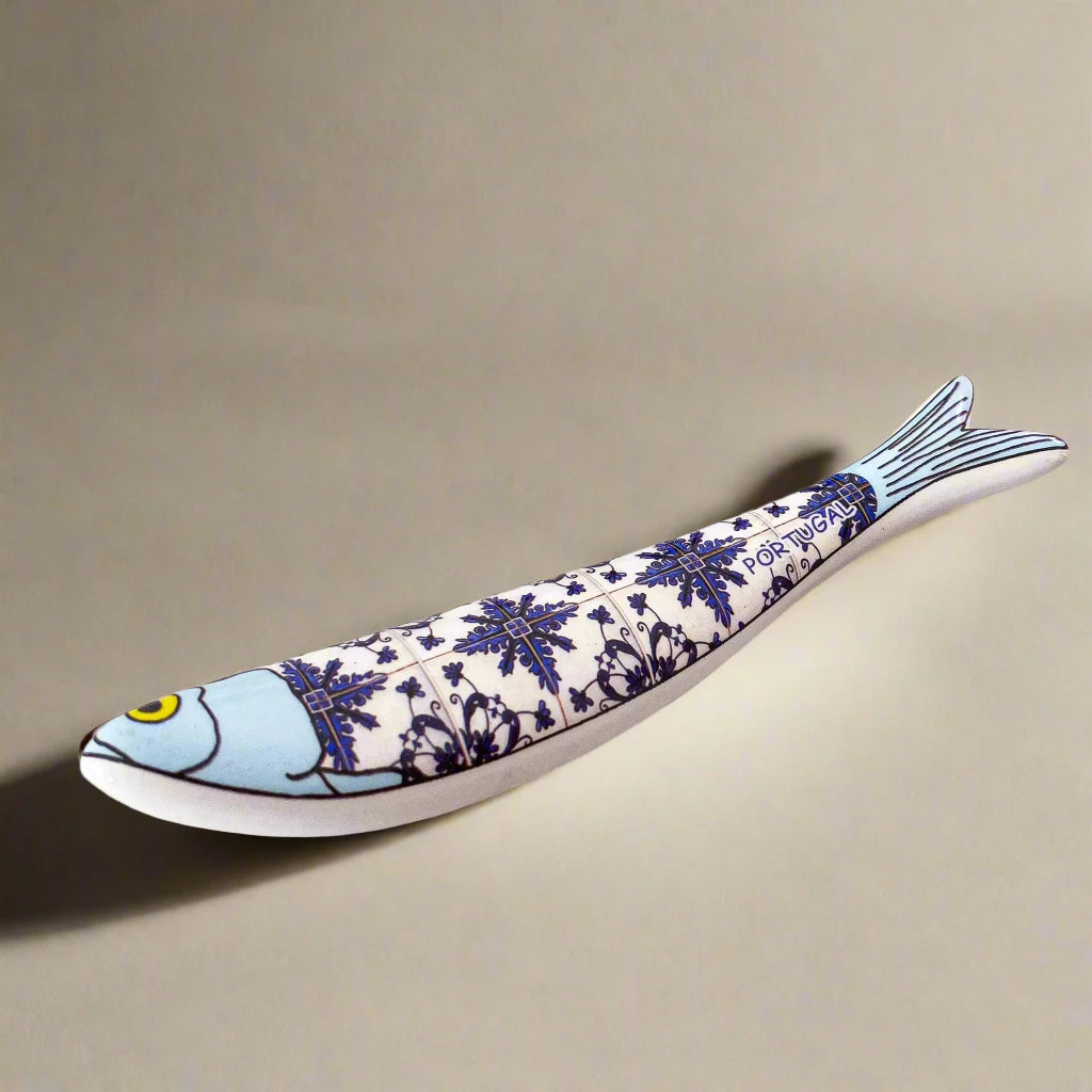 A ceramic sardine figurine featuring a light blue head and tail, adorned with intricate dark blue floral and geometric patterns across its body. The design evokes the classic style of traditional Portuguese azulejos tiles, making it a perfect keepsake or souvenir from Portugal.