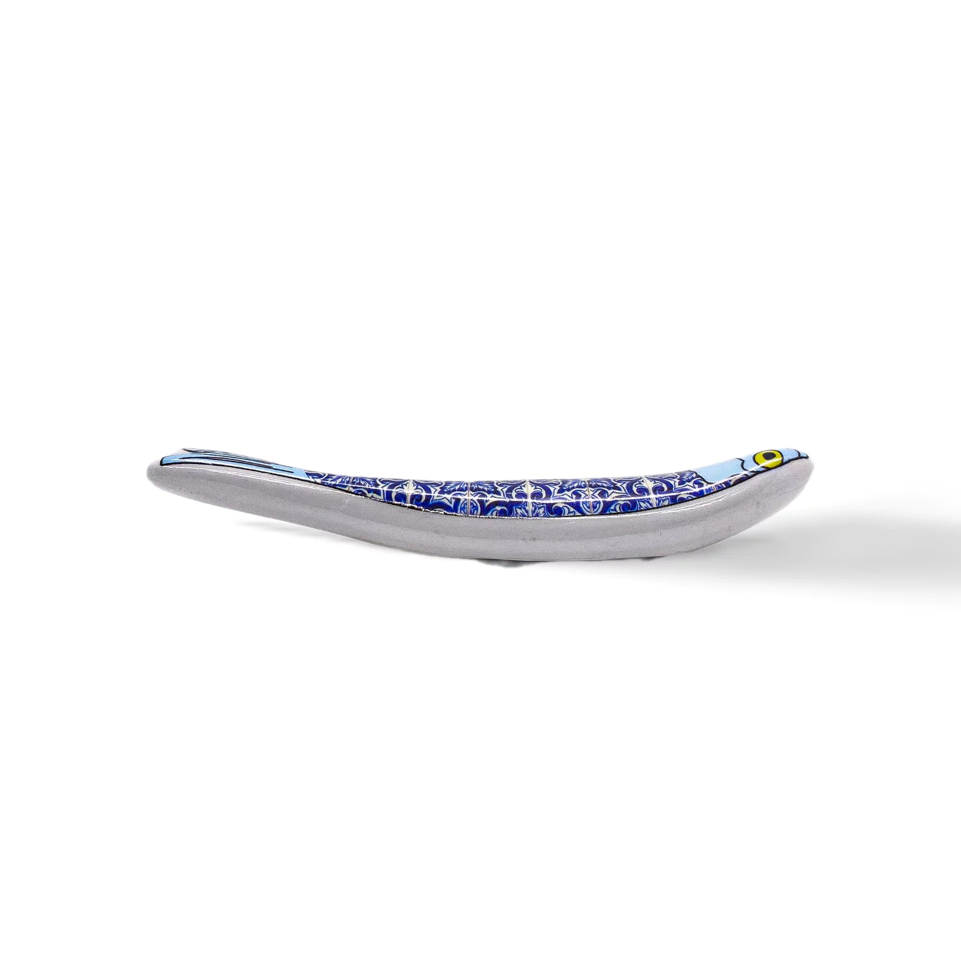 A small, white sardine-shaped sculpted figurine stands upright against a plain white background. Featuring two large, circular, dark indents resembling eyes, the smooth and minimalist design gives it a modern look, making it an ideal souvenir from Portugal.