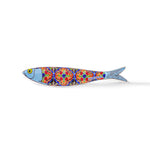 A stylized ceramic fish magnet featuring a blue head, yellow eye, and an intricate, colorful body pattern resembling traditional Portuguese tiles. The vibrant reds, blues, and yellows on its body showcase the word "Portugal" near the tail. This charming souvenir is isolated on a white background.