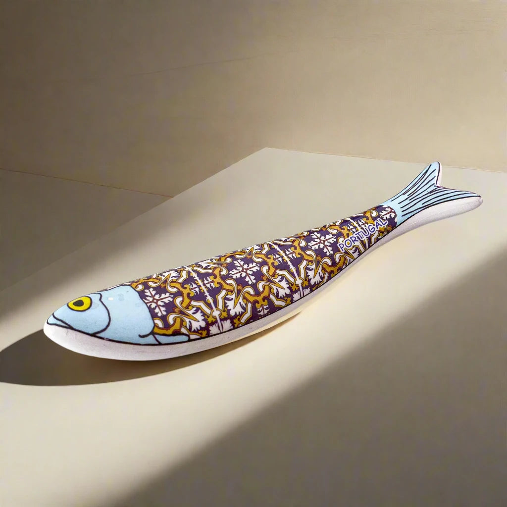 A stylized fish sculpture, inspired by the iconic Portuguese sardine, showcases a blue head and a body adorned with intricate patterns in yellow, white, and purple. The fish has a prominent yellow eye and a light blue tail that subtly blends into the background, making this vibrant piece a striking magnet as well as a beautiful decorative item.