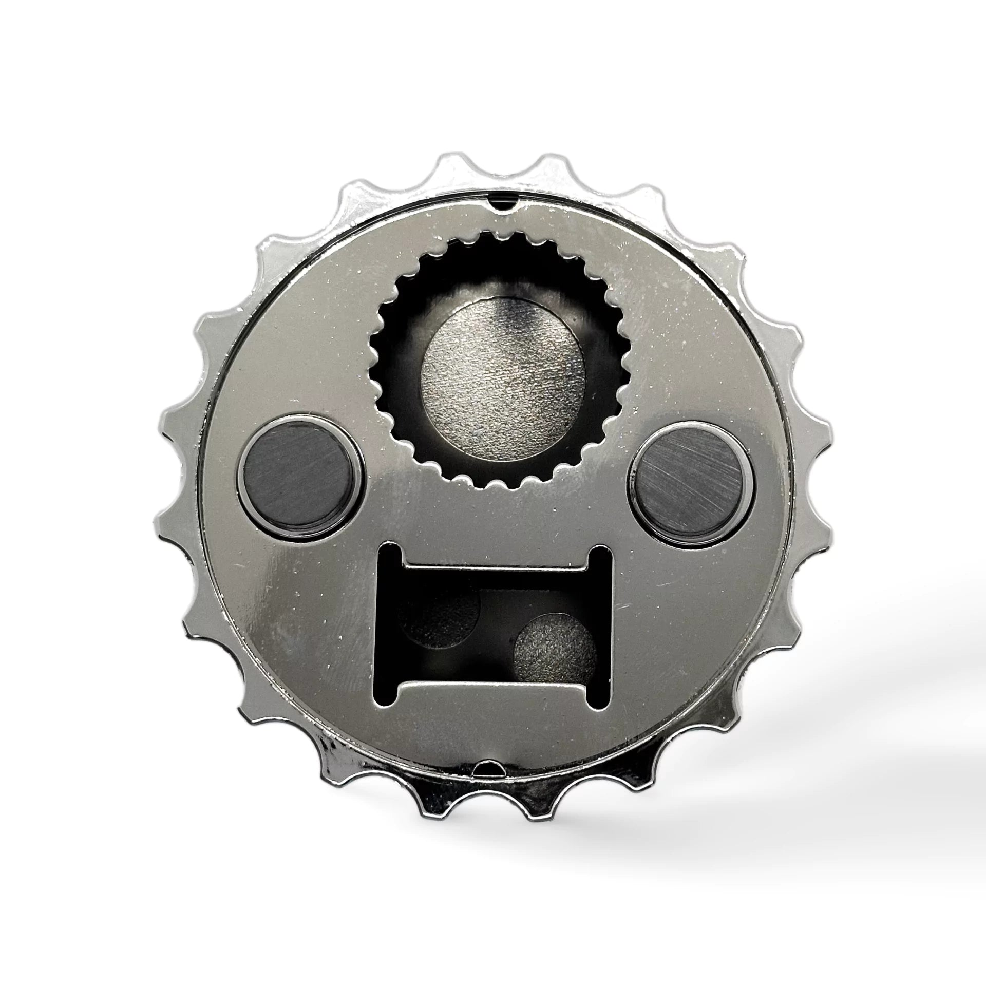A close-up image of a mechanical part resembling a gear or cogwheel with a circular shape and multiple small teeth around the edge. The gear features three distinct circular compartments and a rectangular slot, giving it a face-like appearance, much like a quirky magnet from Portugal.