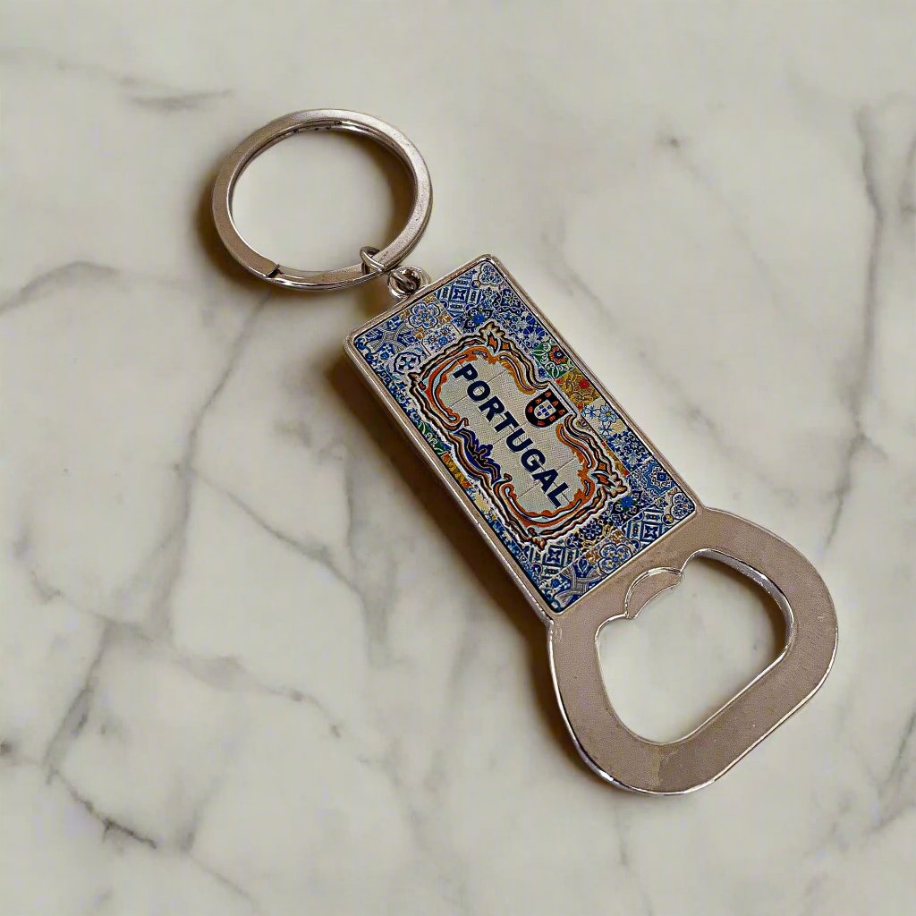 A souvenir keychain featuring a vibrant blue and multicolored enamel rectangular pendant with intricate designs and the word "PORTUGAL" in bold lettering. A convenient bottle opener is attached at the bottom, while the keychain ring is sleek and black, adding a stylish touch to this functional keepsake.