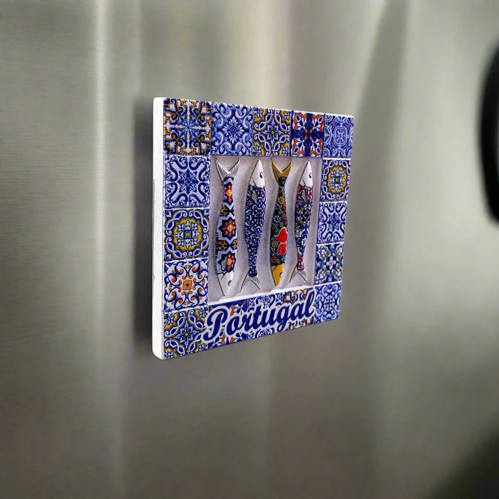 A decorative tile magnet showcases four fish with vibrant, colorful patterns, placed over a detailed blue and white azulejo-style background. The word "Portugal" is elegantly written in blue cursive at the bottom, creating a charming and picturesque souvenir.