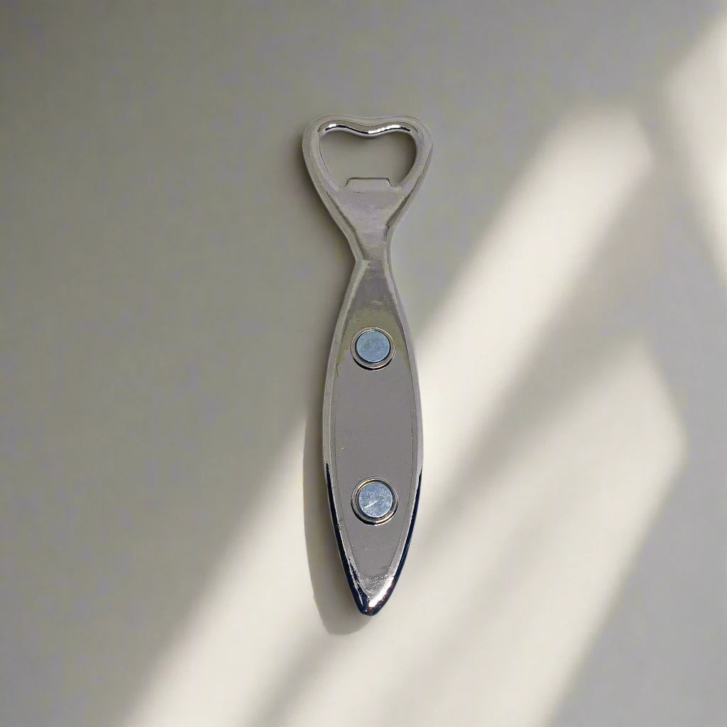This fish-shaped metal bottle opener showcases elaborate blue and white designs that echo Portuguese azulejos tiles. "Portugal" is prominently featured on its side, and a magnet on the back enables it to adhere to your refrigerator. The opener is positioned at the fish's tail end.