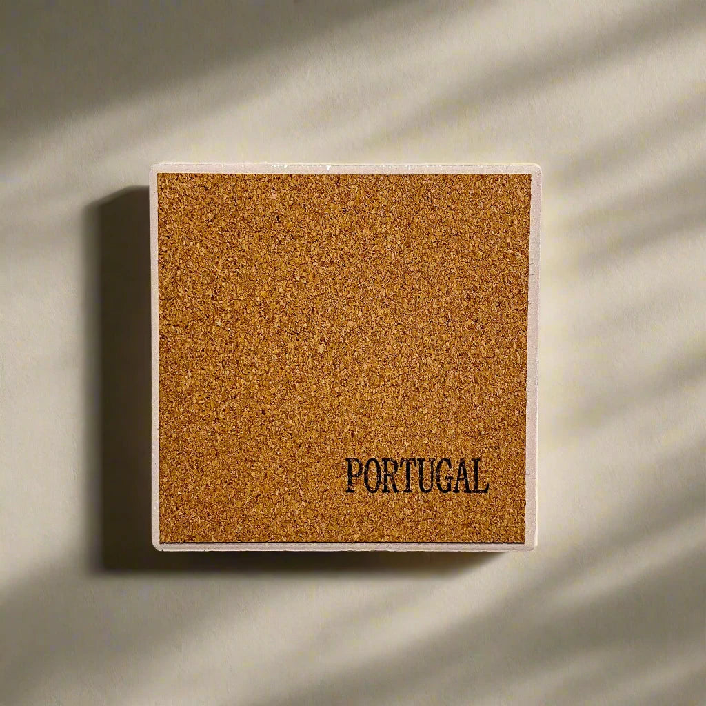 A rectangular cork board mounted on a wall with the word "PORTUGAL" printed in black letters in the bottom right corner, serving as a charming souvenir. Subtle shadows fall across the wall and board, suggesting natural light from a nearby window.