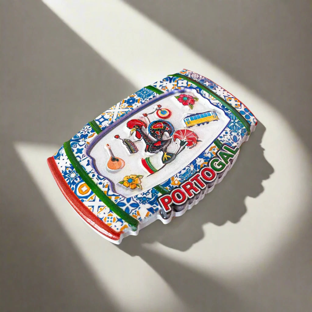 A vibrant magnet adorned with classic Portuguese symbols, including a rooster, traditional musical instruments, flowers, and a tram. The word "PORTUGAL" is boldly featured at the bottom in red, green, and yellow. The background showcases a lively tile pattern inspired by the charming streets of Porto.