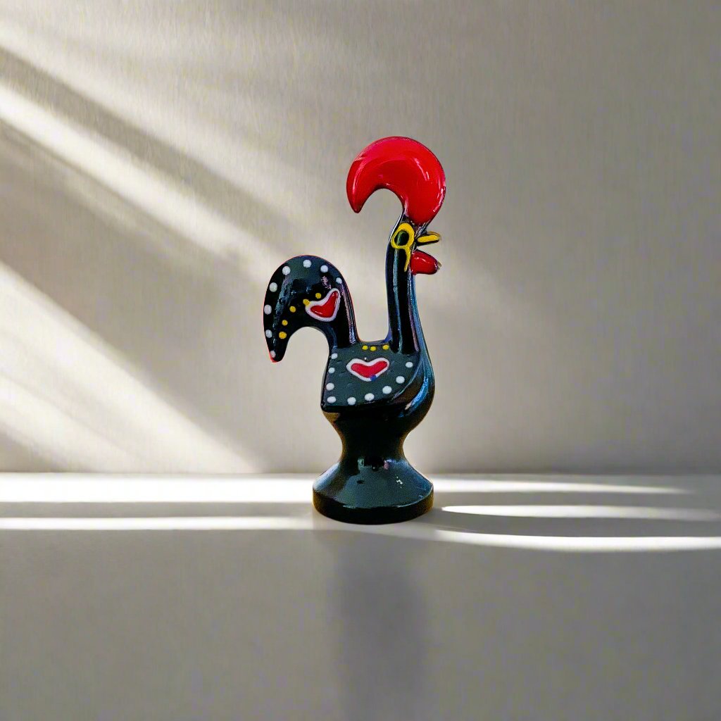 A decorative black and red rooster figurine, representing the Galo de Barcelos, placed on a table as a Portuguese souvenir.