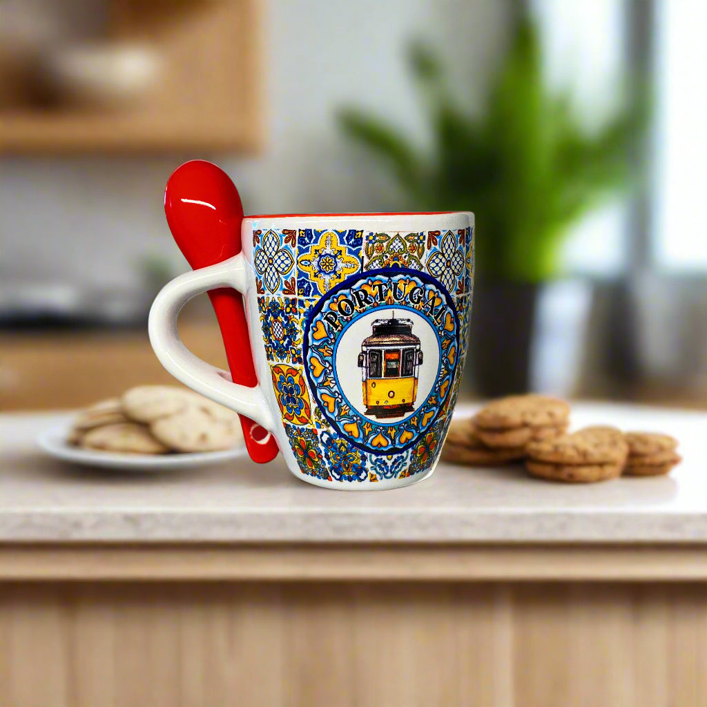 Decorative mug with a tram design and a red spoon on a white surface
