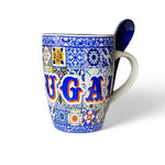 A colorful Portugal ceramic souvenir mug with blue traditional tile motifs, featuring the word 'PORTUGAL' on the front and a dark blue spoon in the handle, presented against a white background.