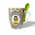 A colorful ceramic mug with a illustration of a yellow tram and traditional tile motifs, accompanied by a green ceramic spoon.
