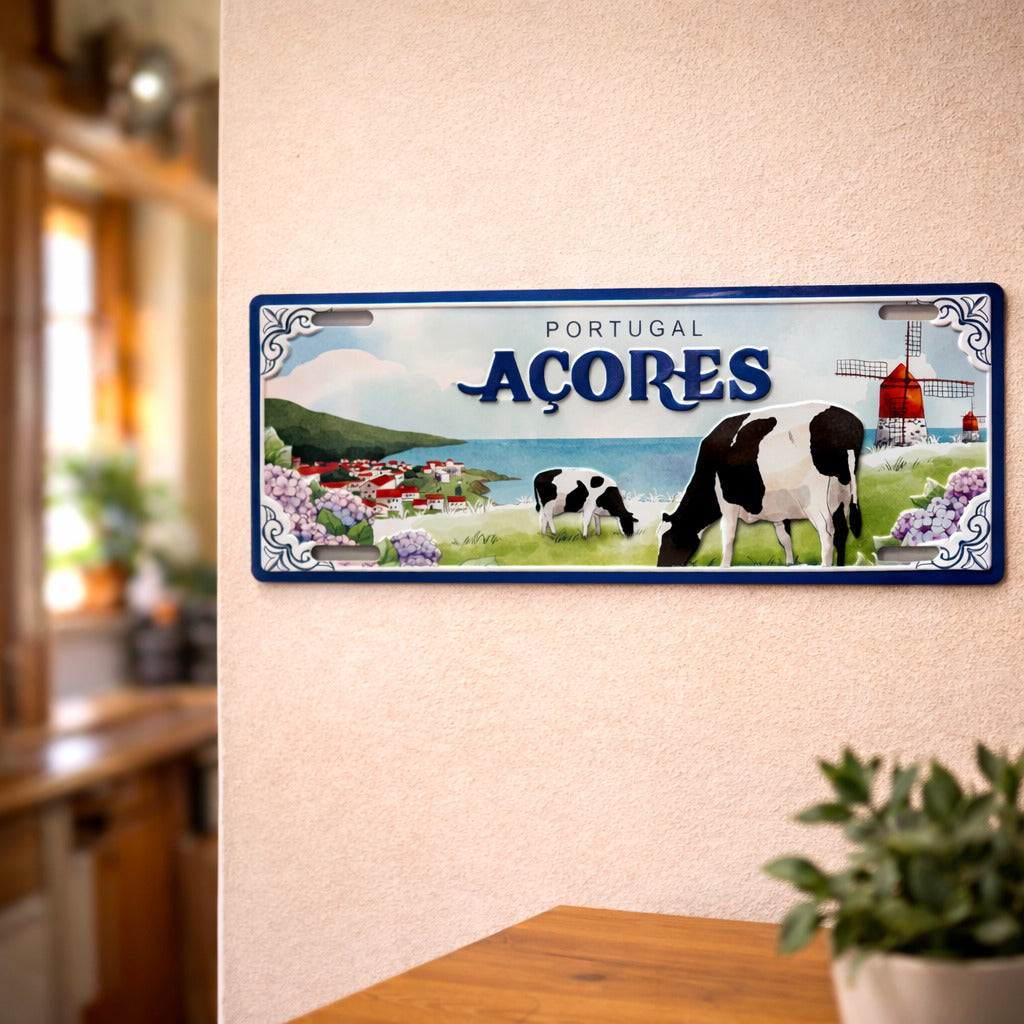 Açores metal souvenir sign mounted on a wall featuring cows, green landscapes, hydrangeas and a traditional windmill