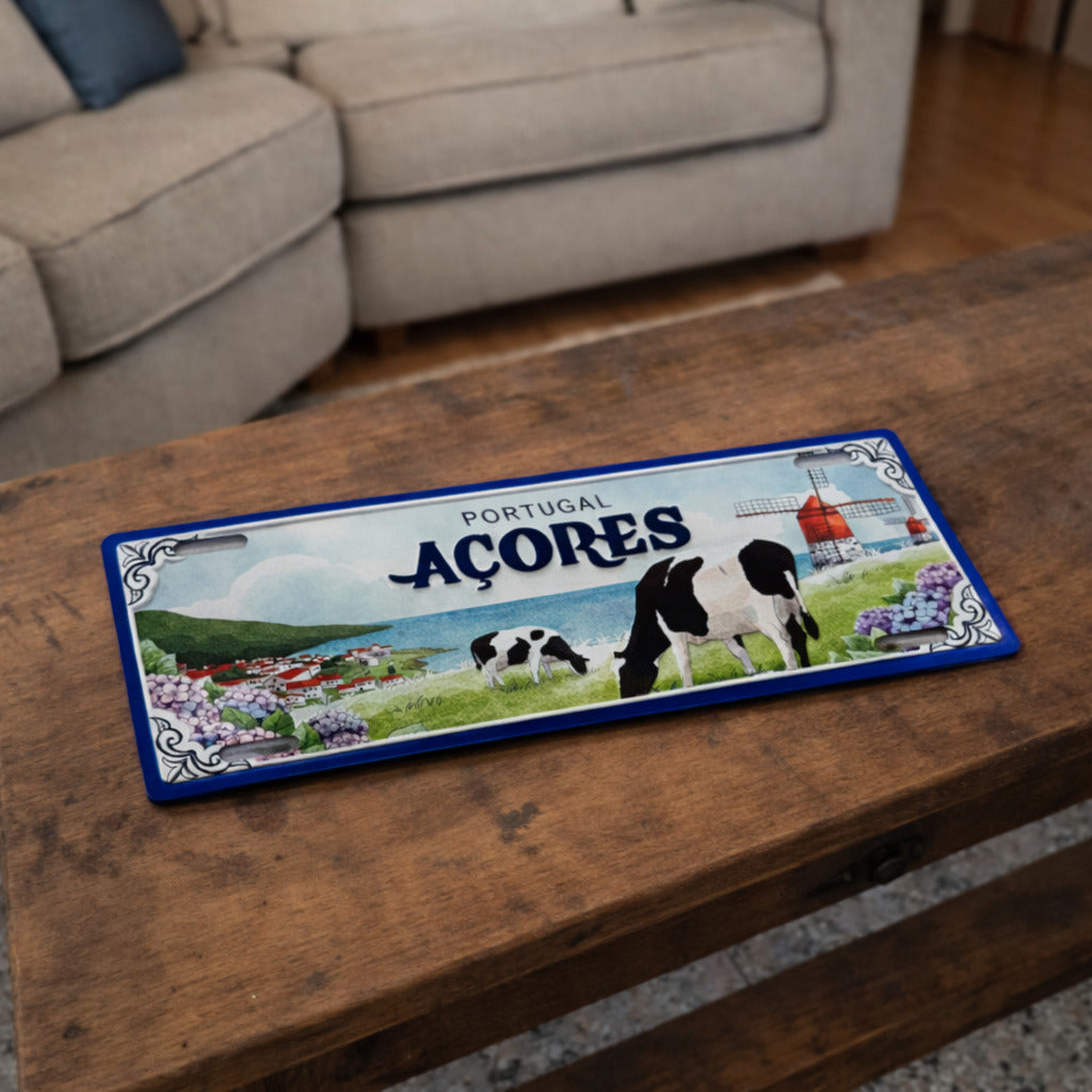 Açores metal souvenir sign placed on a wooden table showing cows, coastal village, hydrangeas and windmill scenery