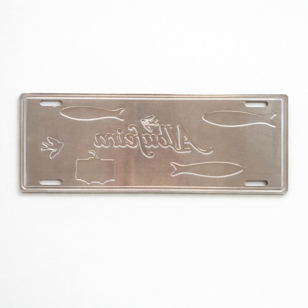 Back side of Albufeira metal souvenir sign showing raw metal surface with cut outlines and mounting slots