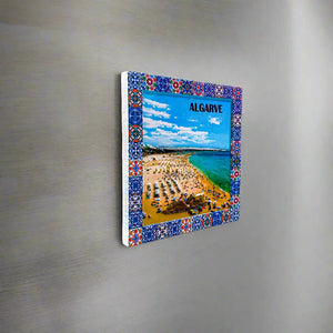 A vibrant ceramic tile with a blue border showcasing an aerial perspective of a bustling beach in Algarve, Portugal. The shore is crowded with people and umbrellas, with a striking turquoise sea and bright blue sky in the background. The word "ALGARVE" stands out clearly at the top.