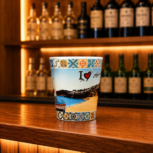 Algarve souvenir shot glass featuring coastal beach scenery and colorful Portuguese azulejo tile patterns displayed on a wooden counter