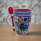 A detailed ceramic mug with a patchwork of intricate, colorful designs featuring various geometric and floral patterns reminiscent of Portugal. The mug has a red interior, a matching red spoon resting in a holder attached to the handle, and evokes memories of a cherished souvenir from the Algarve.