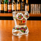 Angled front view of Algarve flamingo tropical bikini style shot glass featuring pink flamingo artwork, tropical foliage patterns, and I Love Algarve text on wooden surface.