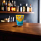 Algarve Portugal souvenir shot glass with colorful regional map illustrations displayed on a wooden bar counter.