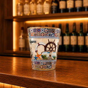 Albufeira Algarve souvenir shot glass featuring nautical wheel, sunglasses, lifebuoy, and colorful Portuguese tile artwork displayed on a wooden counter