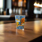 Colorful Algarve souvenir shot glass with seaside cliffs, nautical elements, and Portuguese tile patterns photographed on a rustic wooden table.