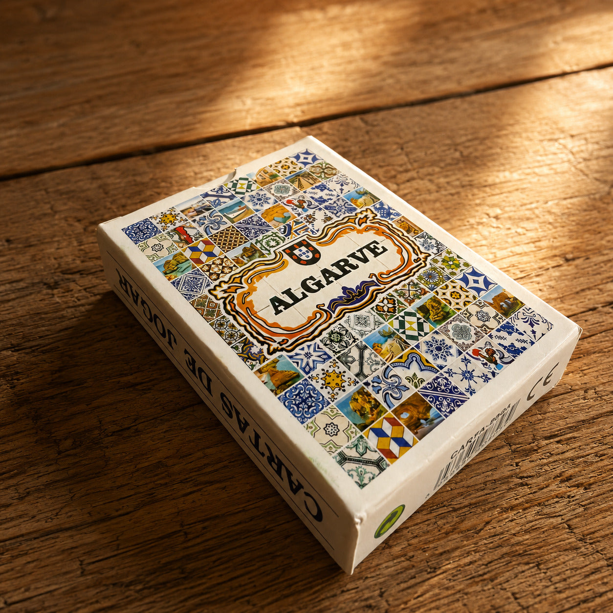 Algarve playing cards souvenir box with traditional Portuguese tile design, photographed on a rustic wooden table with warm natural light.