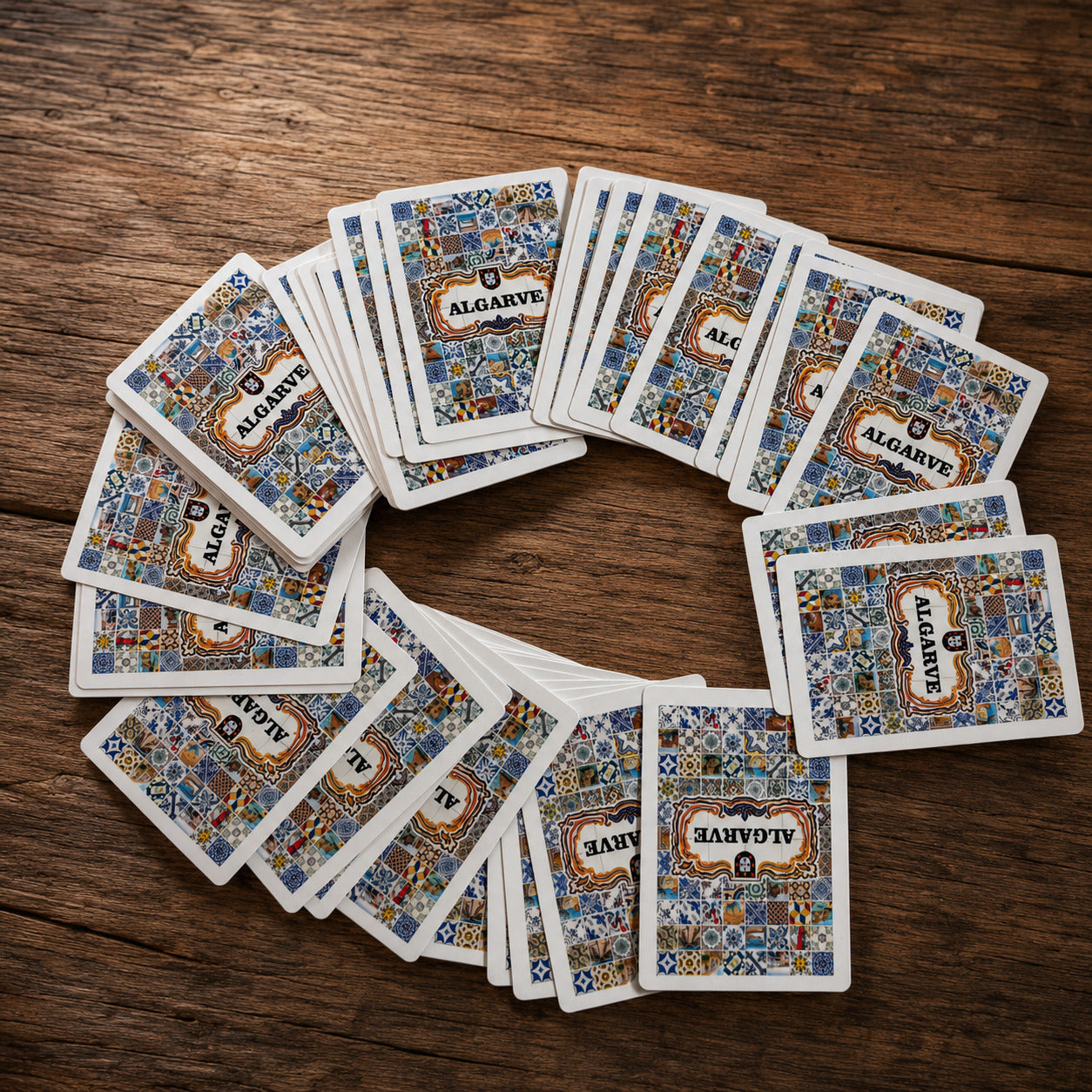 Algarve playing cards souvenir deck spread in a circular arrangement on a rustic wooden table, featuring Portuguese tile-inspired card backs.