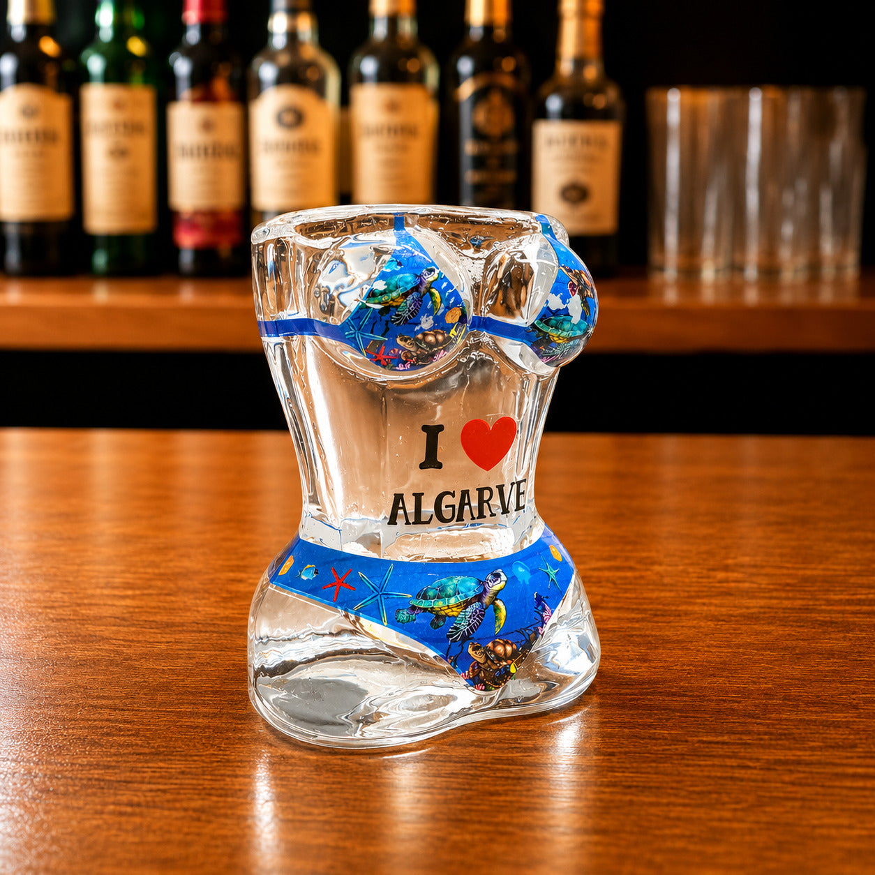 Angled front view of Algarve sea turtle ocean bikini style shot glass featuring marine life illustrations, sea turtles, underwater artwork, and I Love Algarve text on wooden surface.