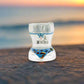 A see-through shot glass featuring a torso shape with a bikini illustration, adorned with beach and ocean scenes. The glass is marked with "I ♥ Algarve" in black and red text on the front, serving as a perfect memento from the Algarve area.