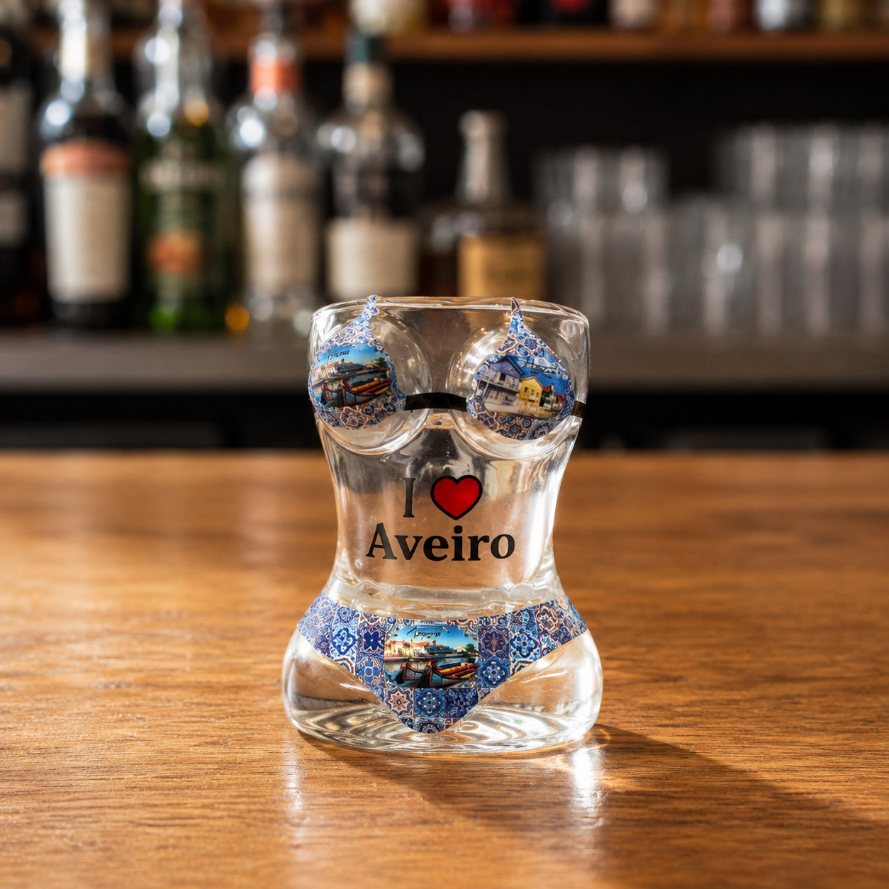 Front view of Aveiro women bikini style shot glass with Portuguese azulejo artwork, moliceiro boat illustrations, and I Love Aveiro text on wooden bar counter.