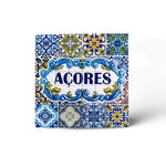 A square decorative tile featuring intricate blue and yellow patterns surrounding the word "ACORES" in bold blue letters. The tile has a traditional, ornate design with various floral and geometric shapes, indicative of Azorean or Portuguese style—a perfect souvenir from the Azores.
