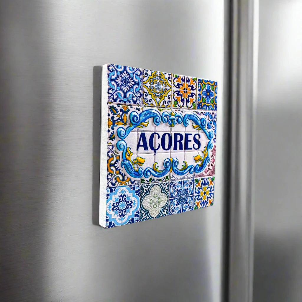 A square decorative tile adorned with detailed blue and yellow patterns framing the word "ACORES" in bold blue lettering. The design features traditional floral and geometric motifs, reflecting the classic Azorean or Portuguese style—an ideal souvenir from the Azores.