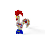 Image of a colorful ceramic rooster figurine known as the Rooster of Barcelos, a cultural symbol and popular souvenir from Portugal. The rooster has red details on its comb, wattle, and heart-shaped accents on its white body, with "Portugal" written on the blue base. Ideal for use as a decorative magnet.