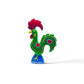 A brightly colored, decorative rooster figurine from Portugal, featuring a green body adorned with red hearts and white dots, a red comb and wattles, and a blue base with the word “Portugal” inscribed on it. This charming piece also functions as a magnet, making it an ideal souvenir.