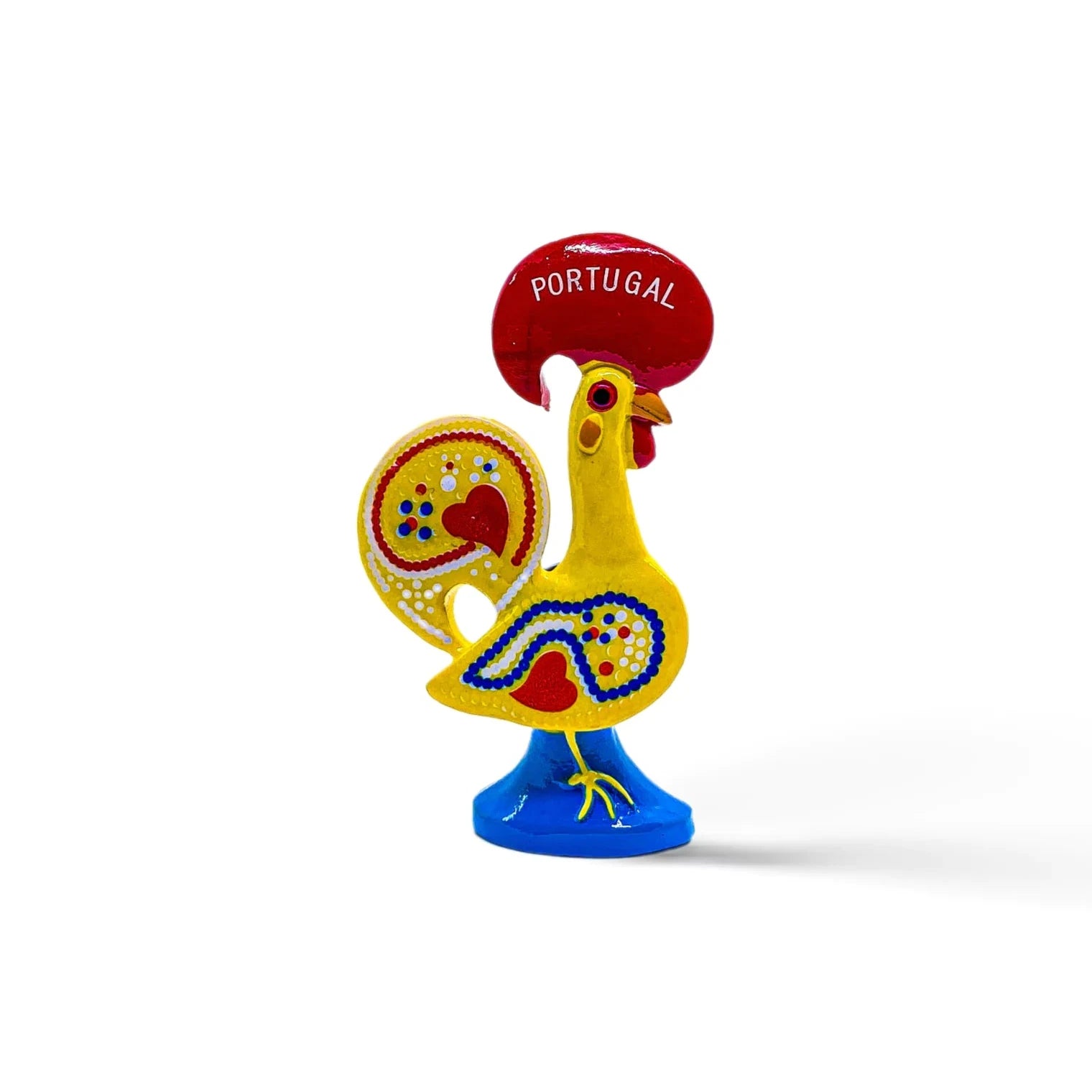 A colorful ceramic rooster figurine with intricate red, blue, and yellow patterns, standing on a blue base. The rooster has a red comb and wattle and is inscribed with the word "Portugal" on the comb, signifying it as a representation of the Galo de Barcelos. This charming piece doubles as a magnet souvenir.