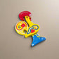 A vibrant ceramic rooster figurine adorned with detailed red, blue, and yellow patterns, mounted on a blue base. The rooster features a red comb and wattle, with "Portugal" inscribed on its comb, symbolizing the Galo de Barcelos. This delightful piece also serves as a magnet souvenir.