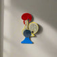 A vibrant ceramic rooster figurine adorned with detailed red, blue, and yellow patterns, mounted on a blue base. The rooster features a red comb and wattle, with "Portugal" inscribed on its comb, symbolizing the Galo de Barcelos. This delightful piece also serves as a magnet souvenir.