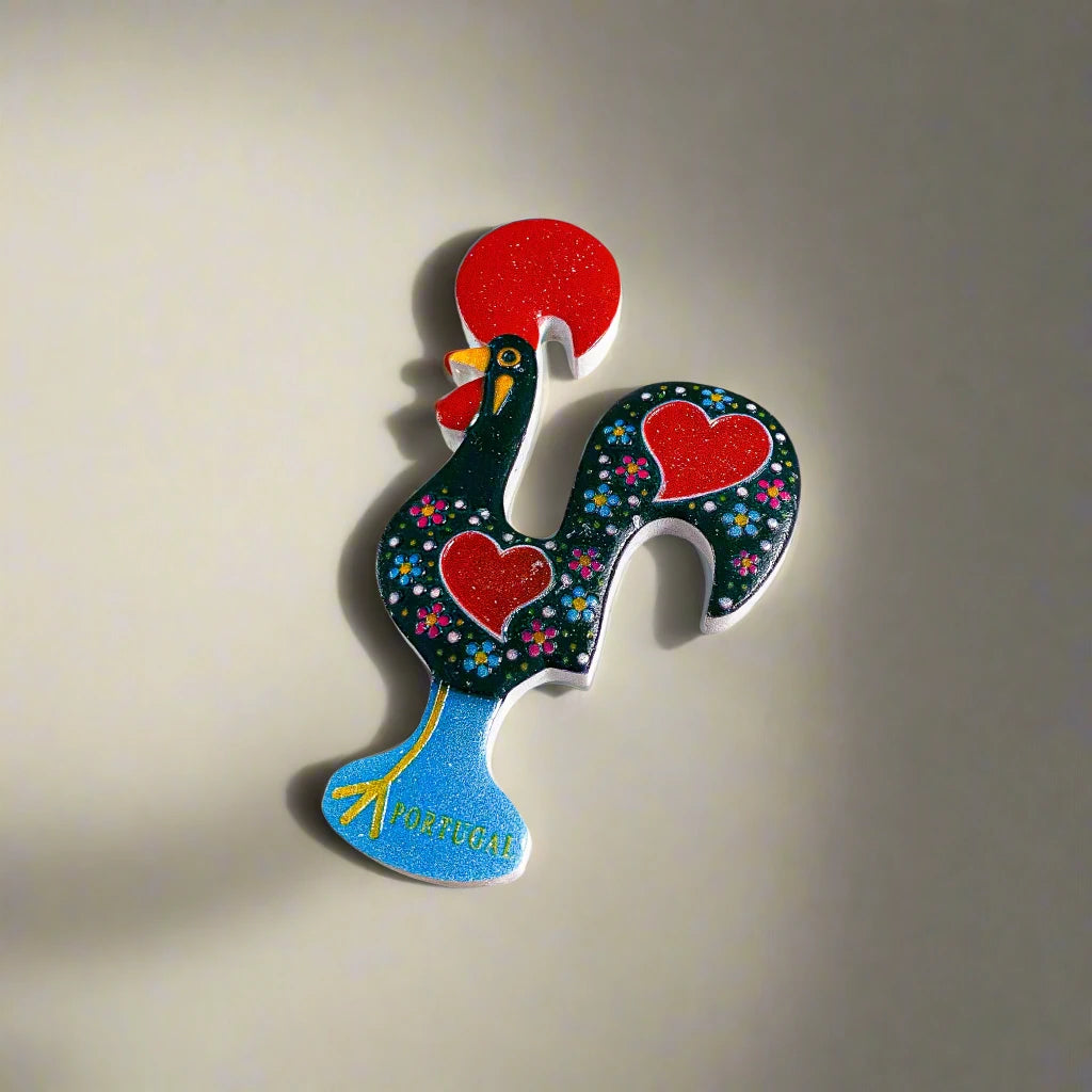 
A lively Barcelos Rooster figurine featuring a black body decorated with red hearts and tiny white dots. It has a red comb, red wattle, and stands on a blue base labeled "Portugal," highlighted by delicate floral patterns, making it a charming souvenir.